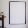 A clean, minimalist blank frame on a neutral-colored wall with a decorative shelf nearby.