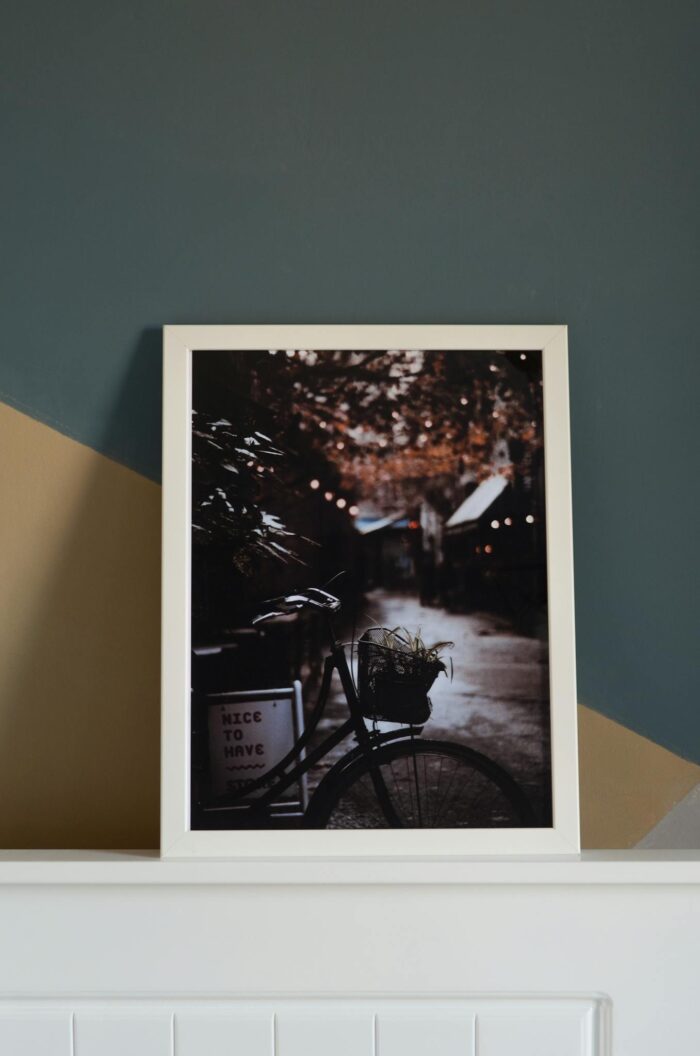 Framed photo of a bicycle in an urban setting with ambient lighting, displayed on a stylish wall.